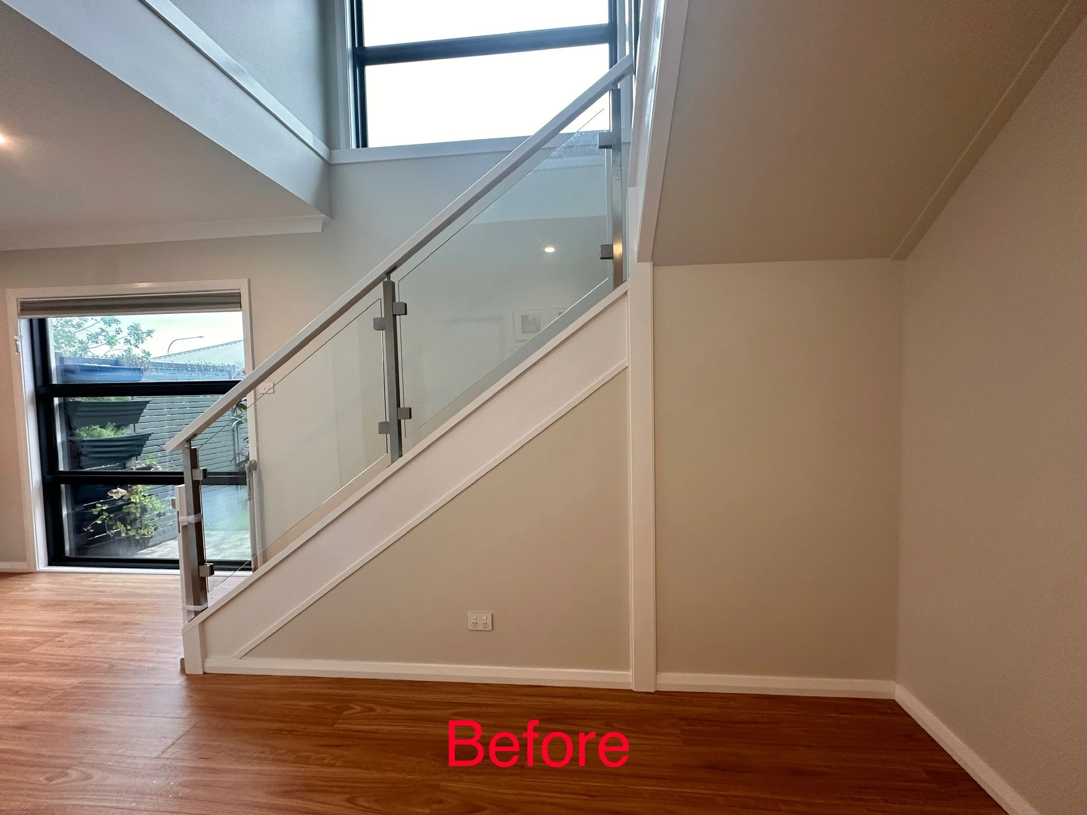 Under stairs space with glass railing and empty wall space before cabinetry installation