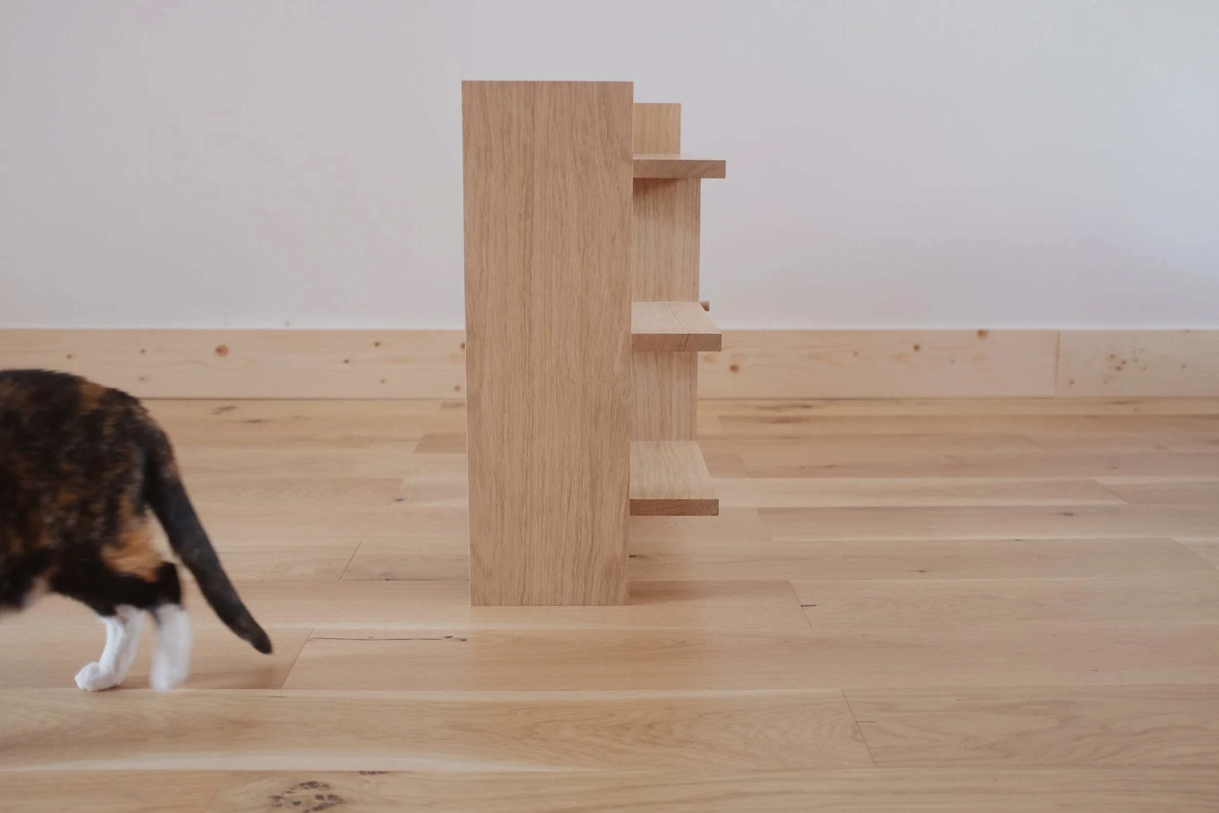 Open shelves on solid oak bedside table with cat to side.