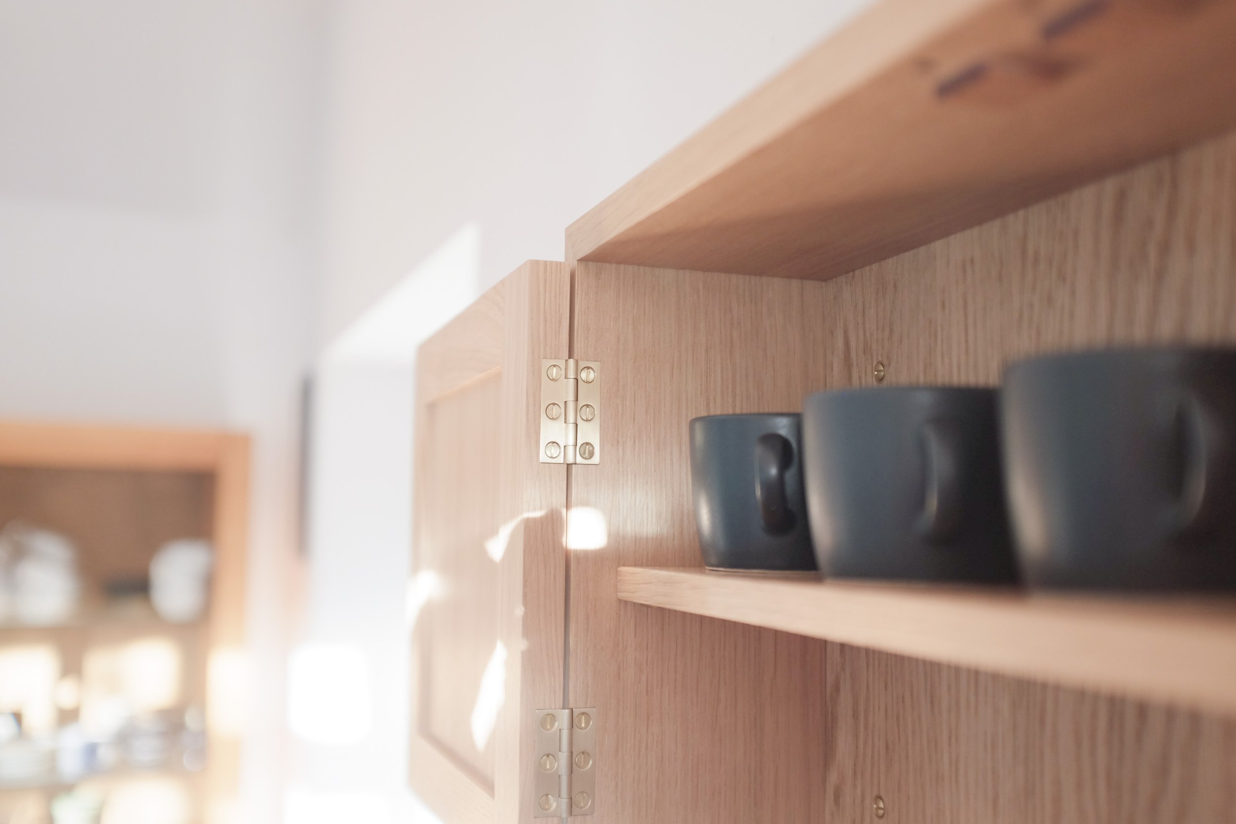 Shadows and light playing across oak wall cabinet containing pottery.