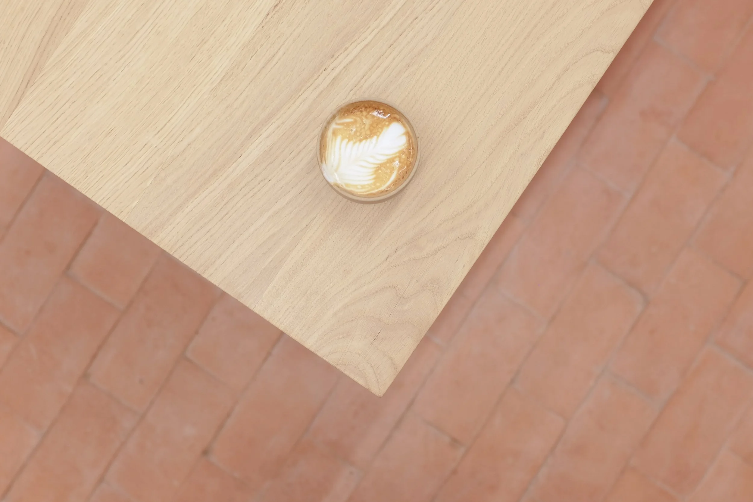 A coffee on the oak Origin table with red terracotta tiles in background.