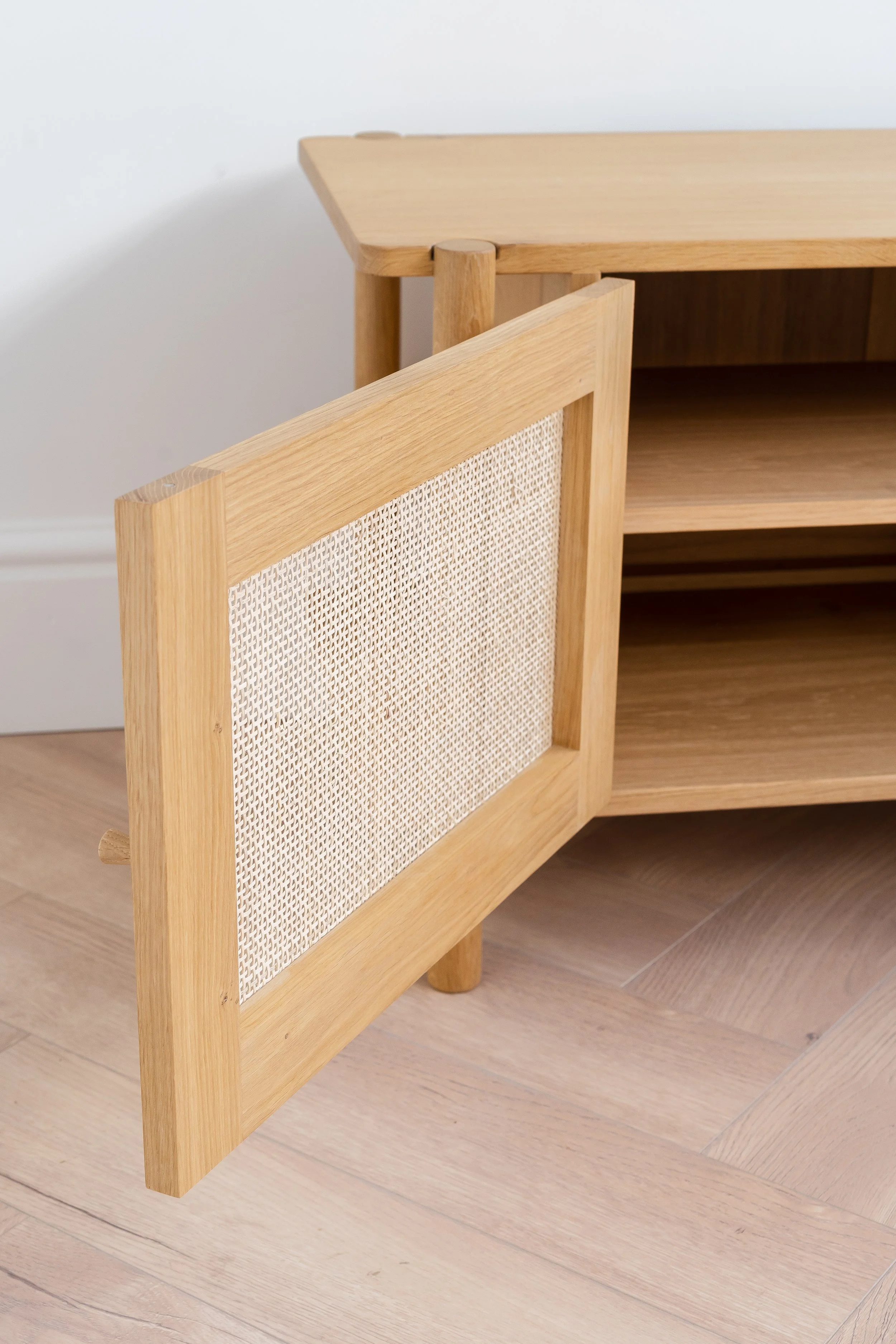 Open door on oak sideboard with woven rattan cane panel.