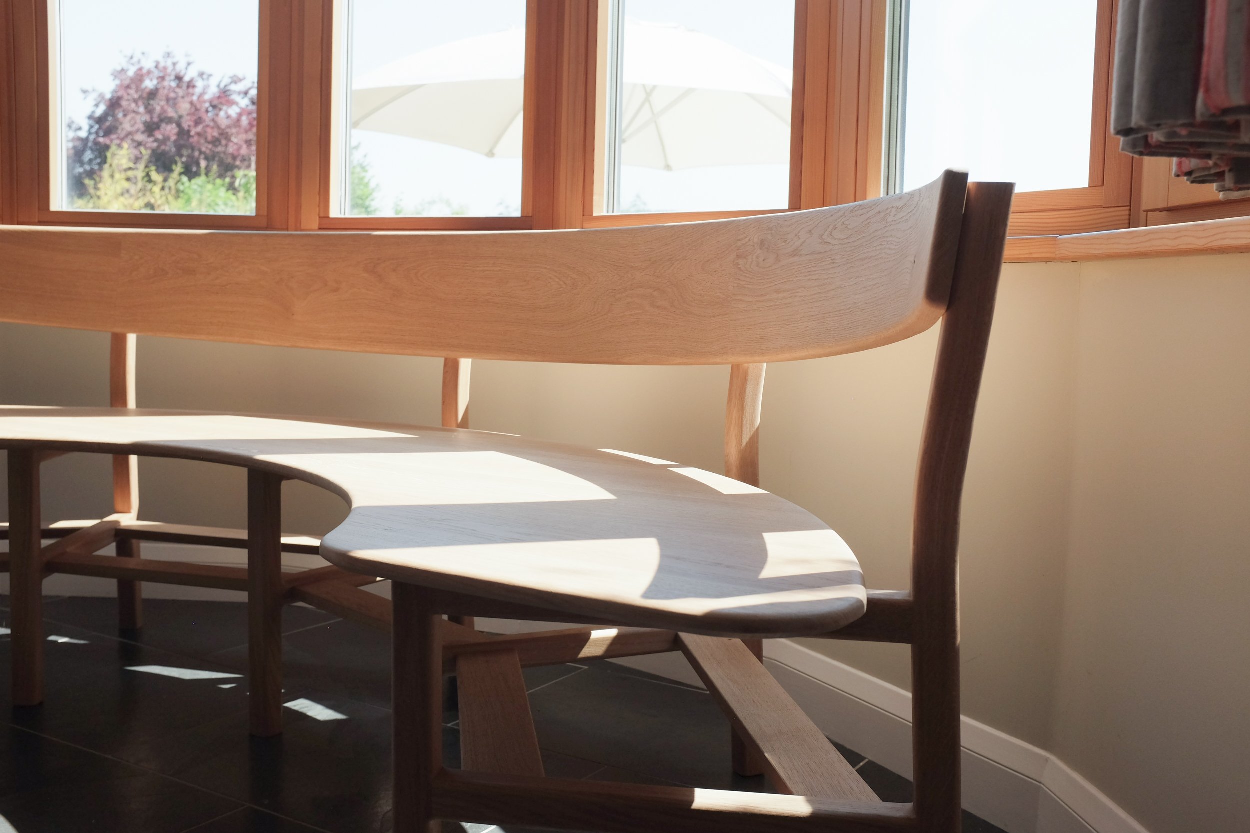 Curved solid oak seat in shadows on the Wye bench.