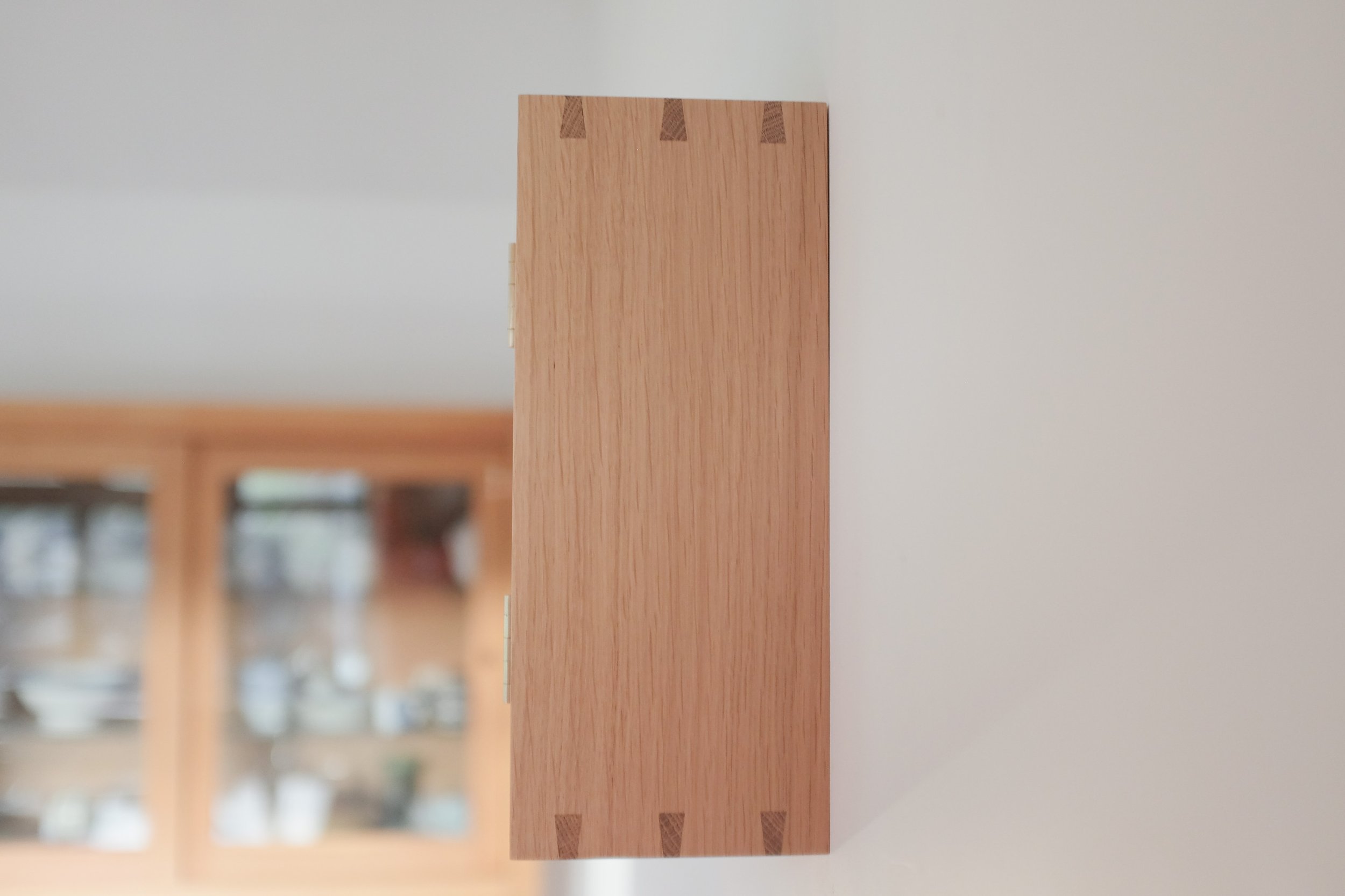 Dovetailed side of oak wall cabinet with oak display cabinet in the background.