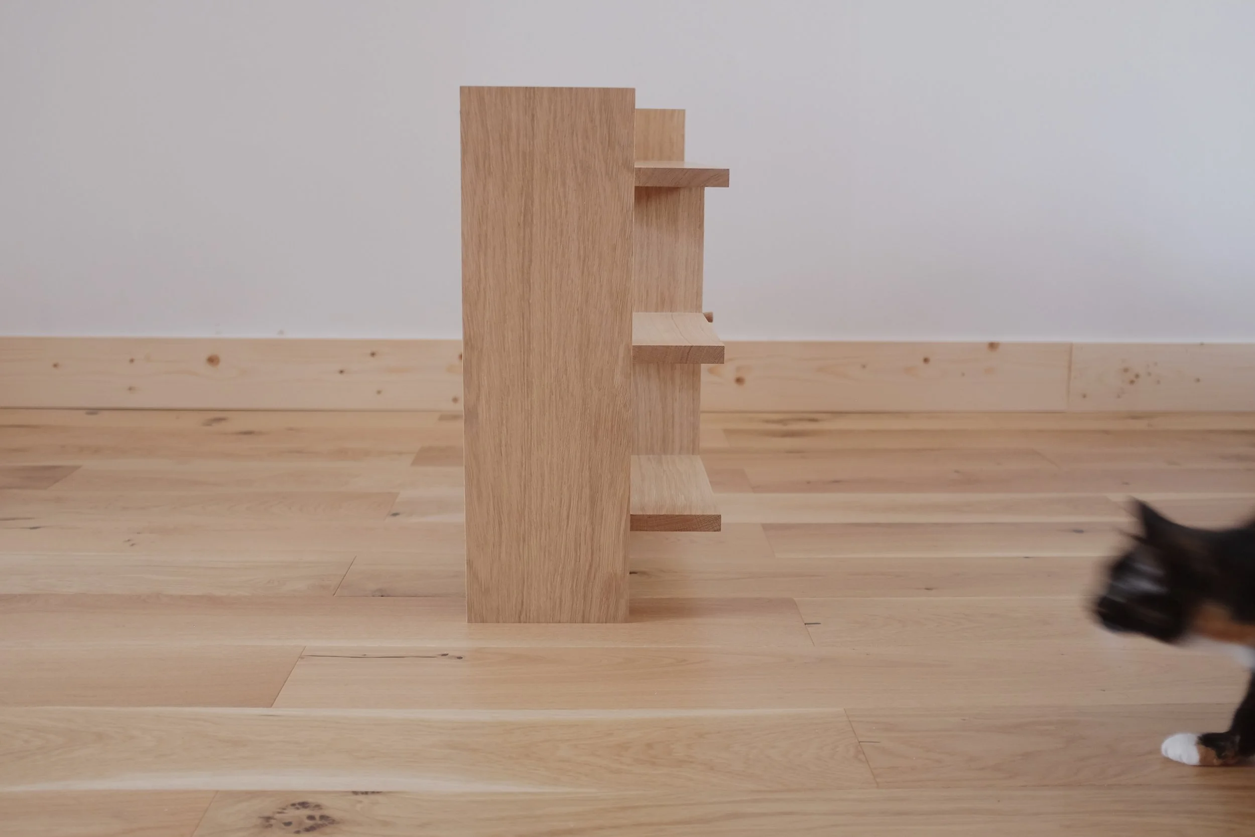 Open shelves on solid oak bedside table with cat to side.