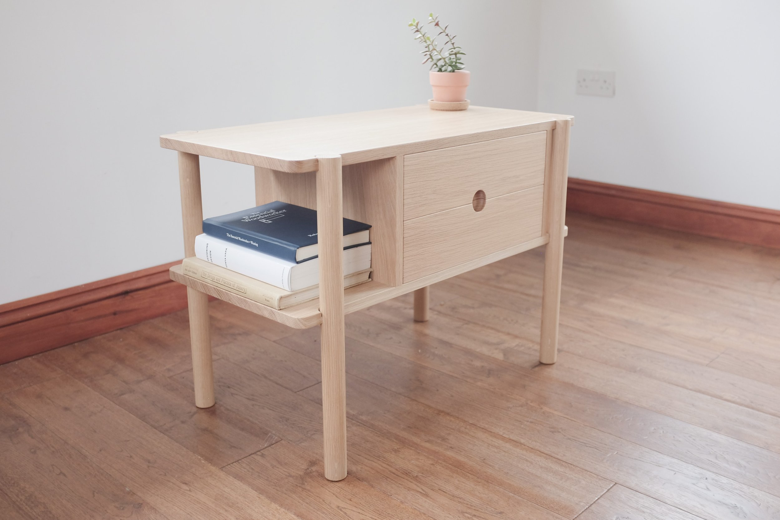 Solid oak bedside table with jade plant in terracotta pot. Books arranged on open shelf of the drawers.