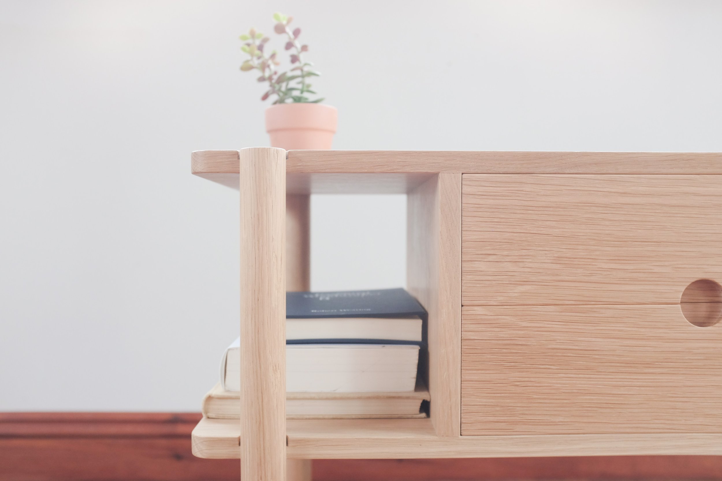 Solid oak bedside table with jade plant in terracotta pot. Books arranged on open shelf of the cabinet.