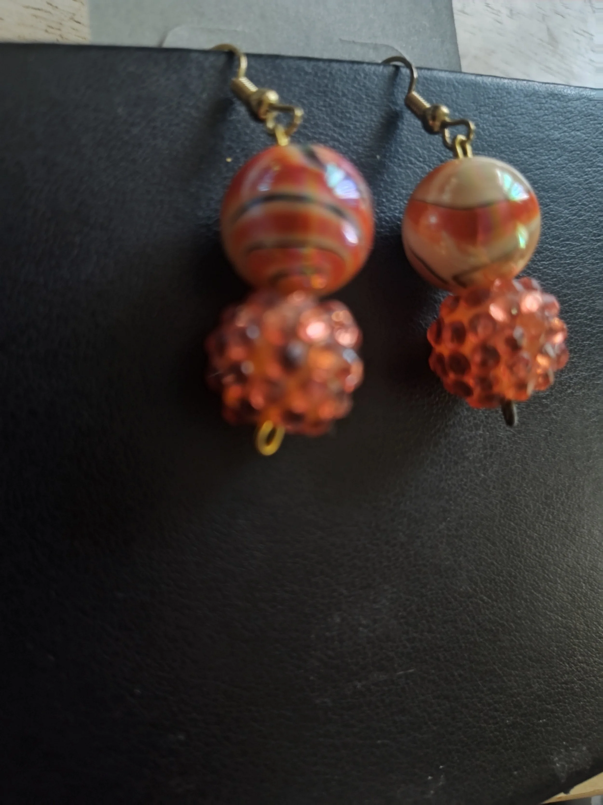 Pair of orange beaded earrings with round beads, some larger and textured, hanging from metal hooks.