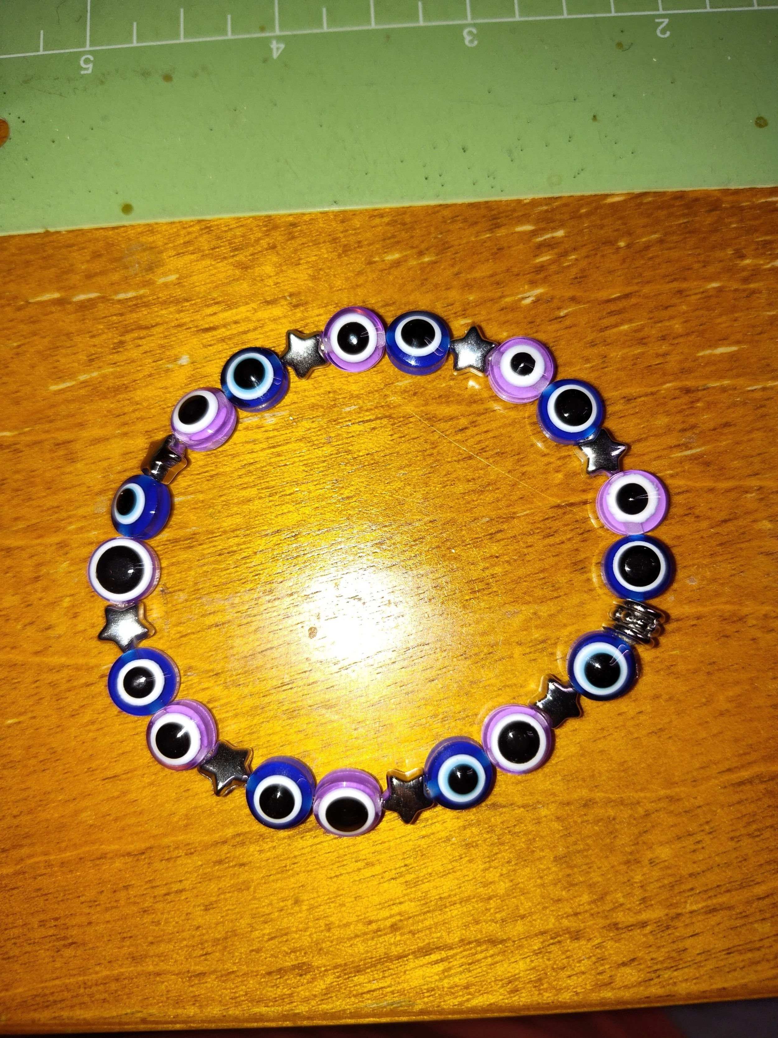 Beaded bracelet featuring blue and purple eye charms and metallic star-shaped beads, arranged in a circle on a wooden surface.
