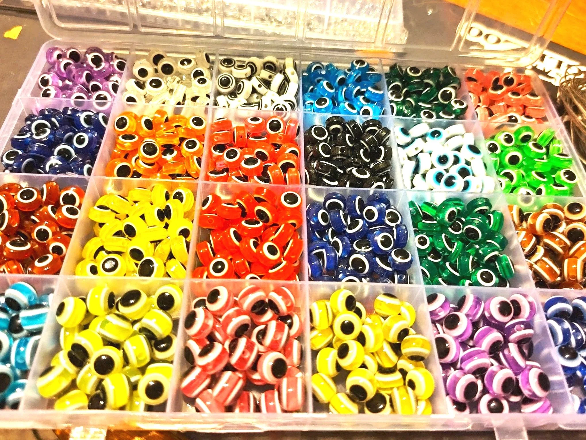 A plastic organizer box with compartments filled with colorful googly eyes used for crafts, arranged in rows with various colors including purple, white, black, blue, green, red, yellow, and brown.
