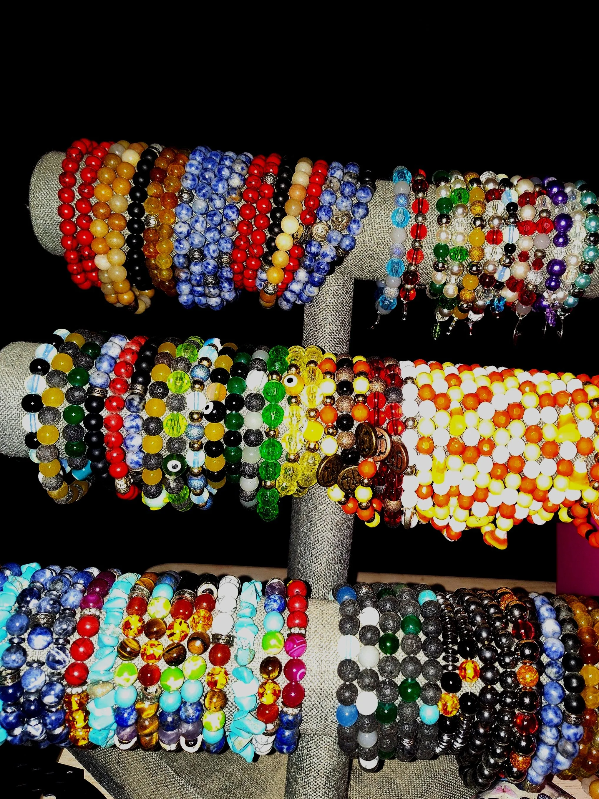 Display of colorful beaded bracelets arranged on a multi-tiered jewelry stand with a black background.
