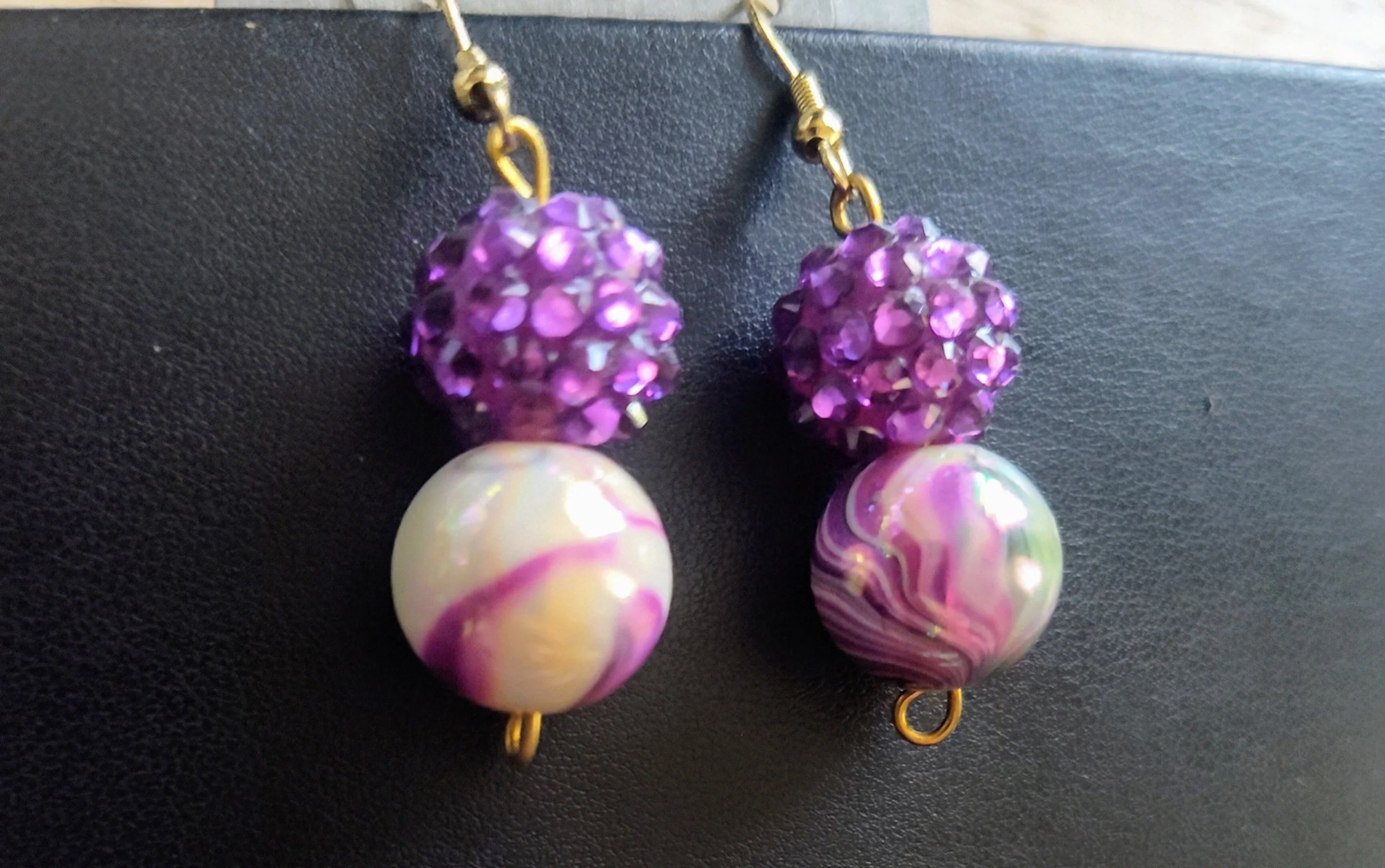 Purple and white beaded earrings with purple rhinestone accents on a black background.