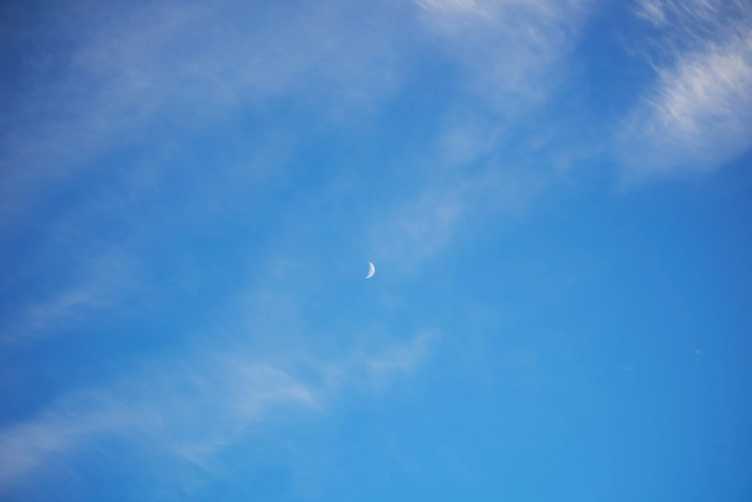 A small crescent moon surrounded by wispy clouds in a blue sky.