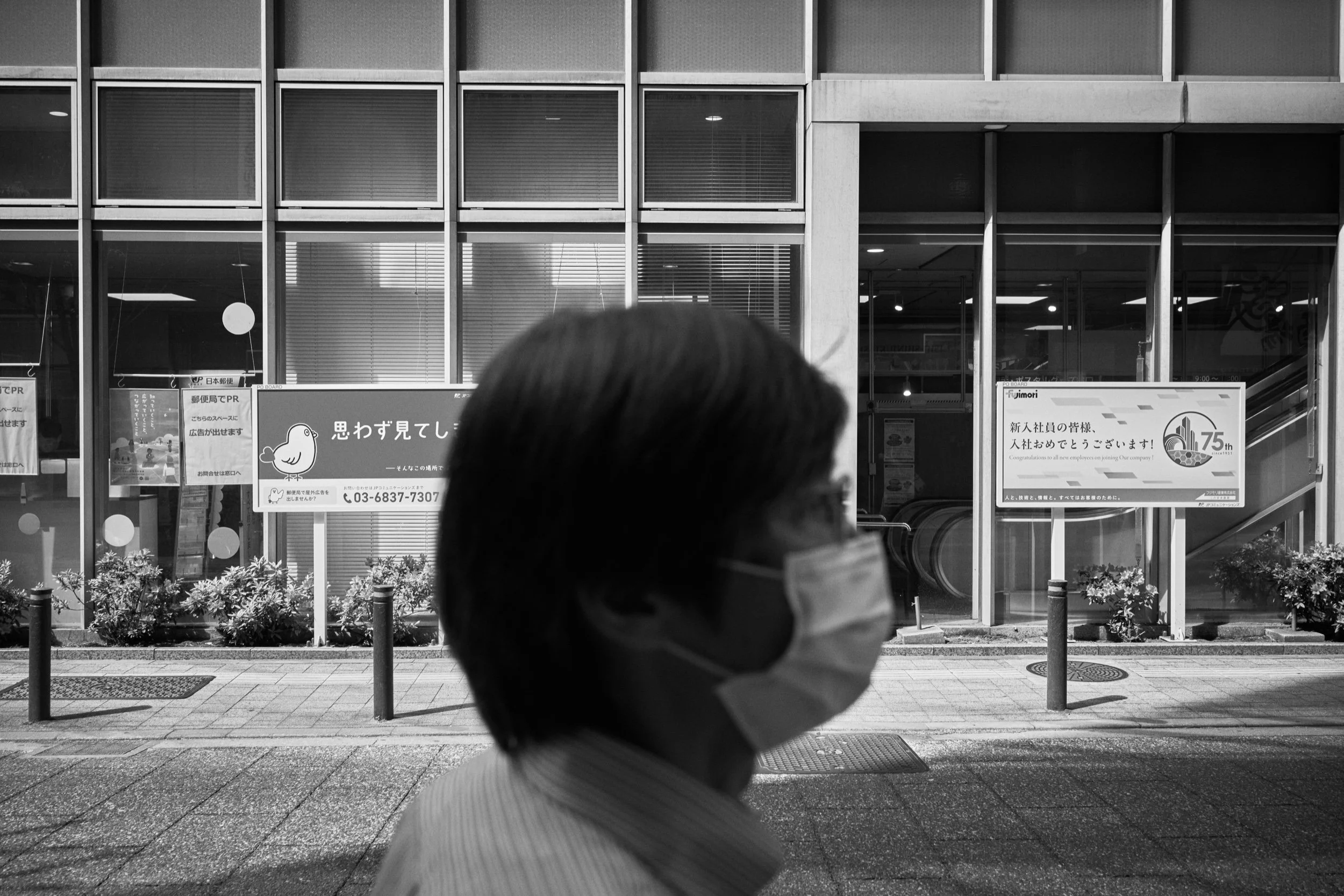 A masked pedestrian passes a post office. Shinjuku, Tokyo.