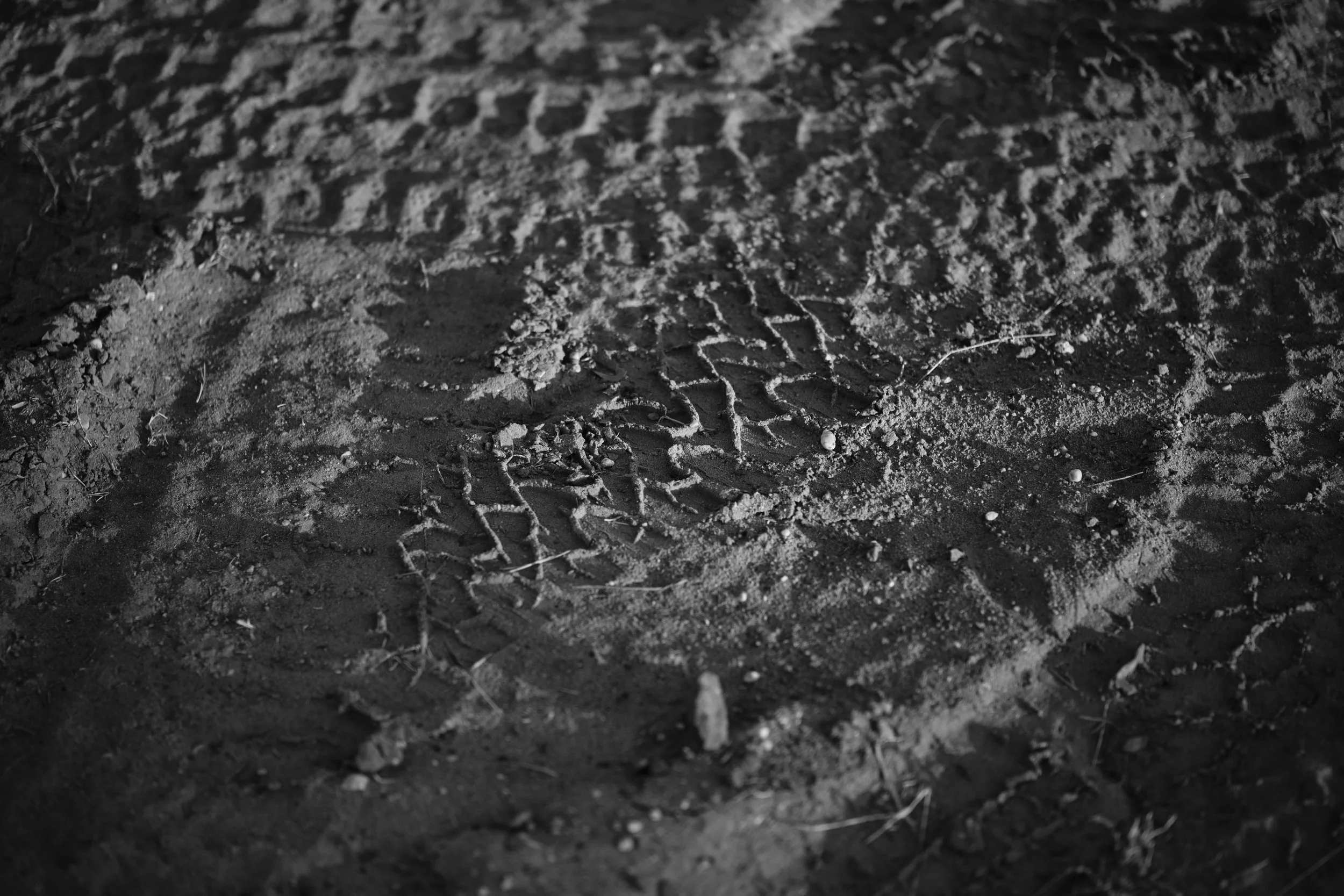 Close-up of tire tracks and footprints on dirt ground, black and white photo.