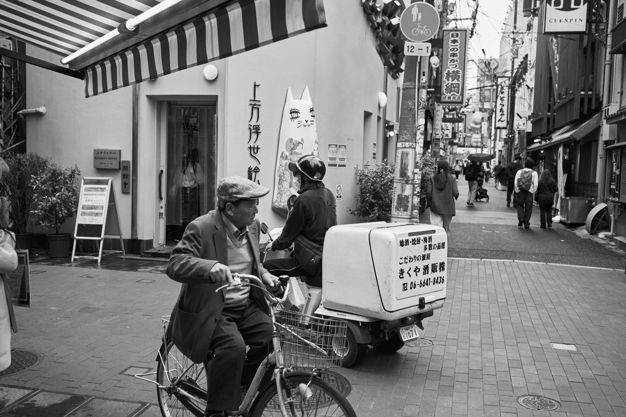 A cyclist passes a delivery scooter. Dotonbori, Osaka.