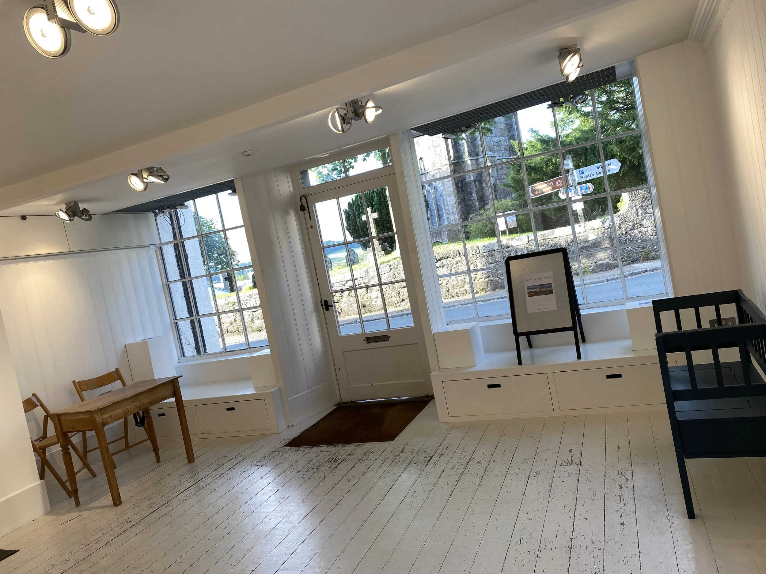 Interior of a bright room with large window, white walls, wooden furniture, and ceiling lights.