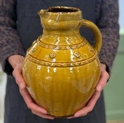 Person holding a yellow ceramic pitcher with a handle and decorative patterns