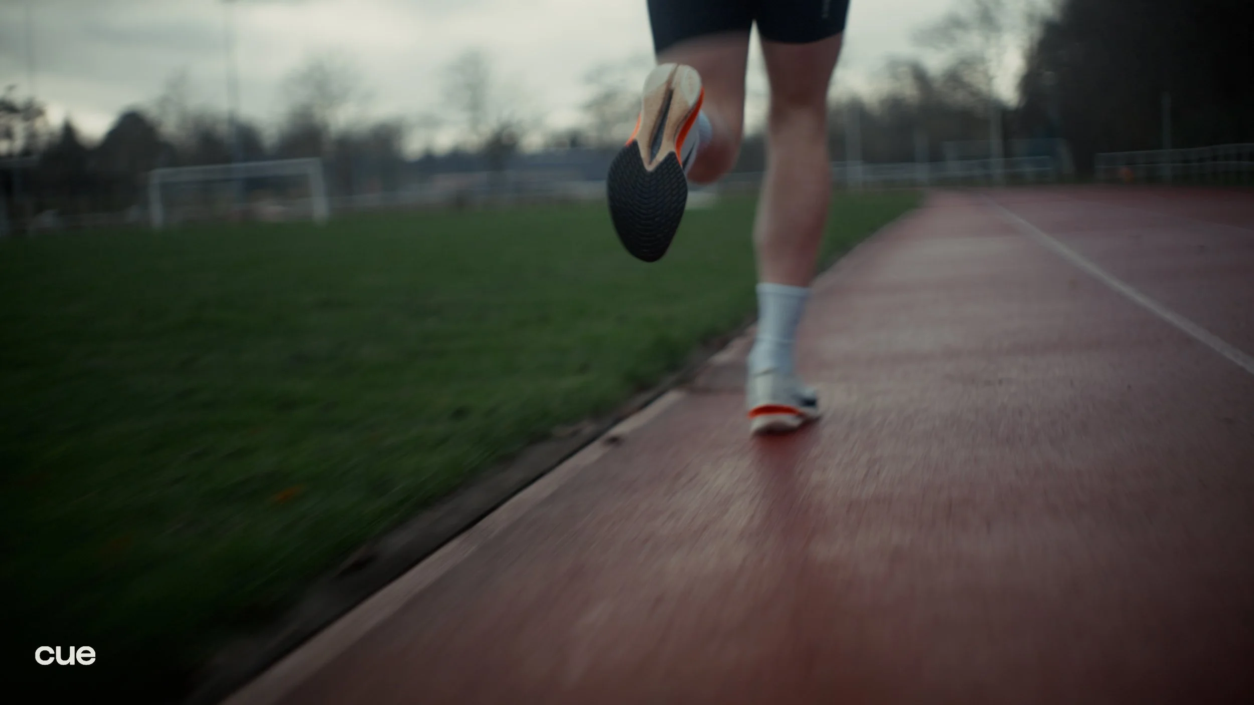 Close-up of a runner's legs and feet on a track, with the focus on the running shoe, as the runner moves forward on an outdoor track field.