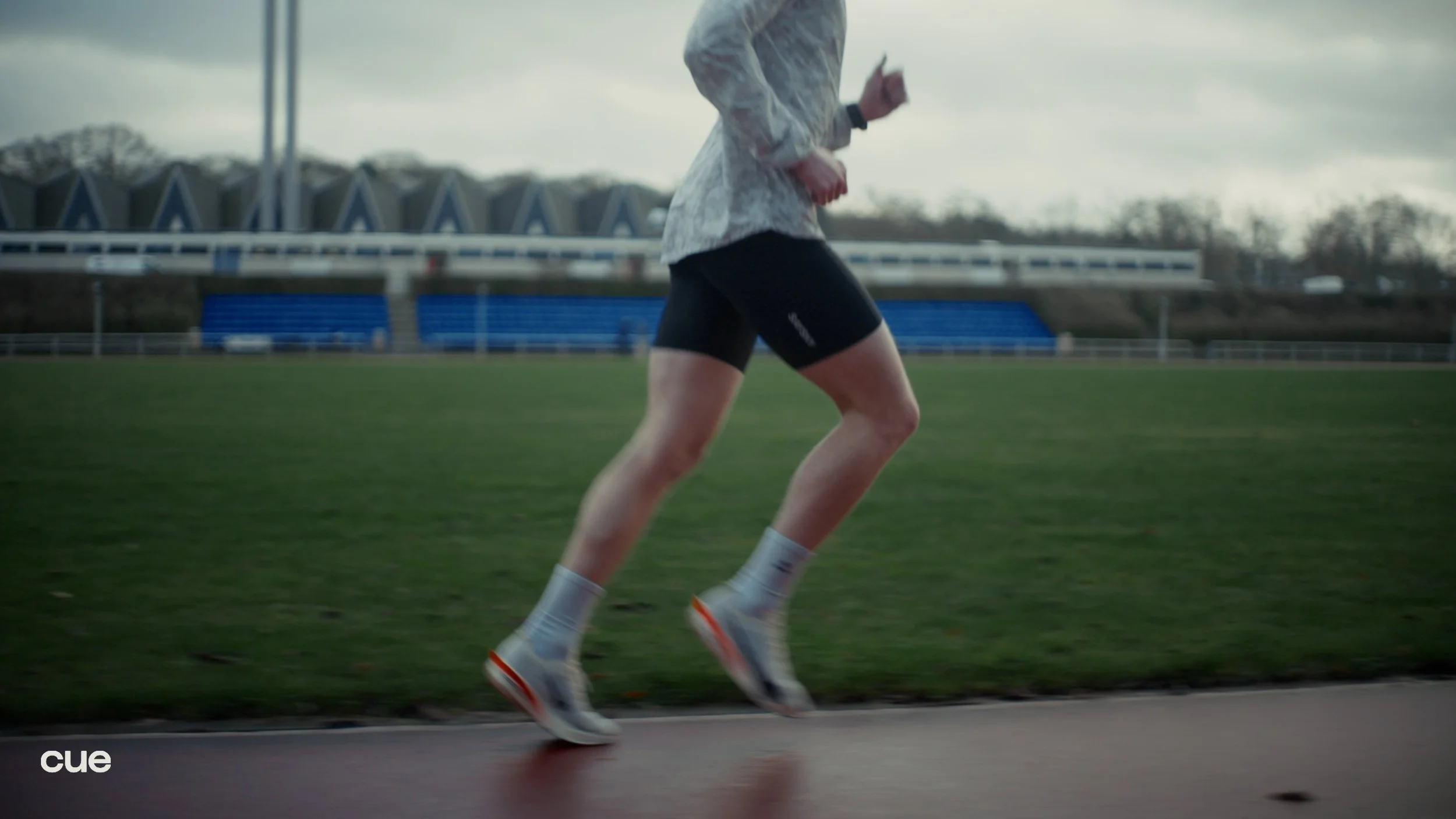 A person running on a track at a stadium with blue seats and a cloudy sky.