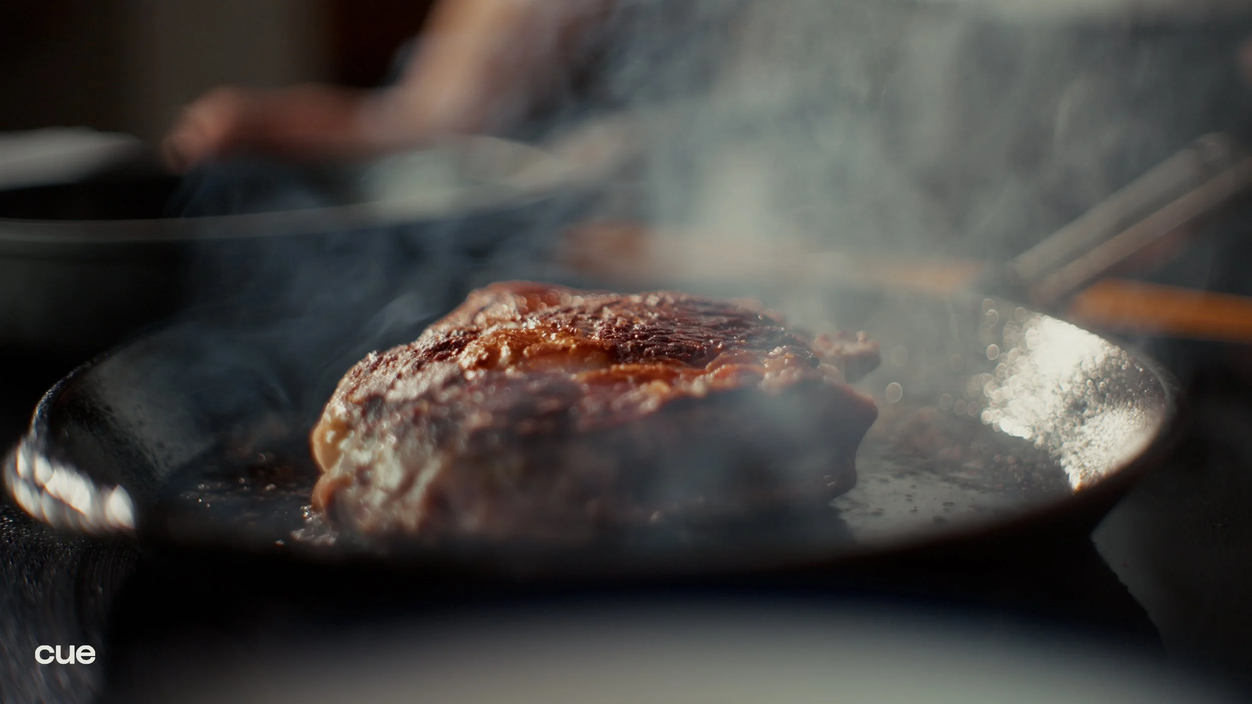 A piece of meat being cooked in a skillet over high heat, with steam rising from it.