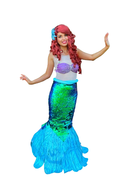 Person dressed as a mermaid with pink curly hair, wearing a purple shell top, a sequined green and blue tail, and a blue flower hair accessory.