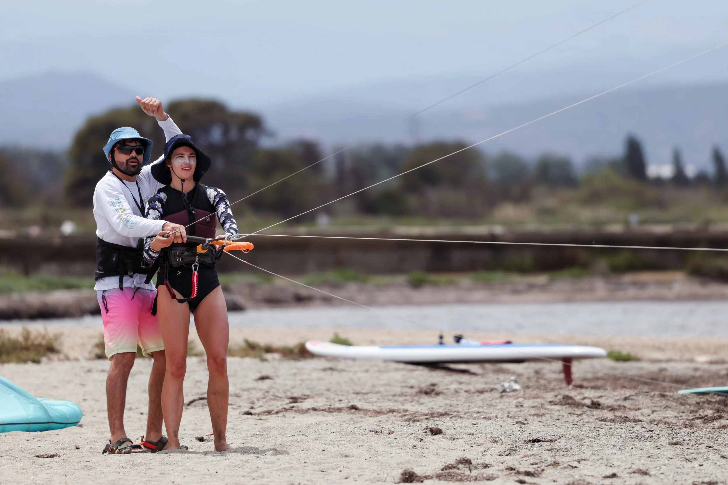 Un profesor de kitesurf esta ayudando su alumna a levantar la cometa en la playa