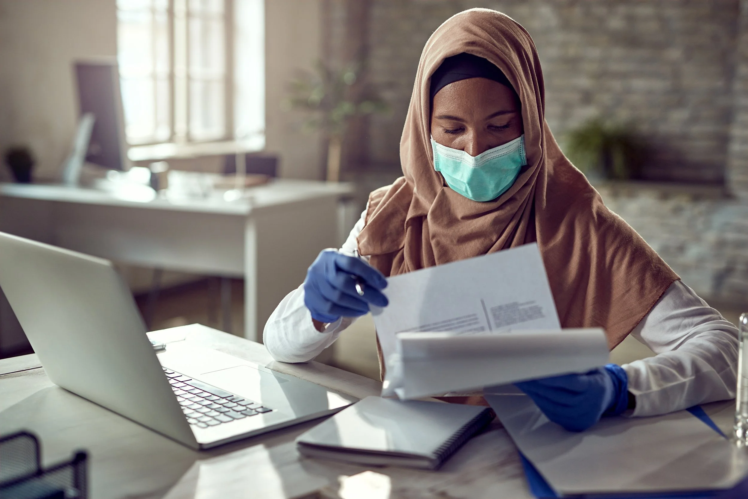 a sited female medical practitioner reading files in front of laptop