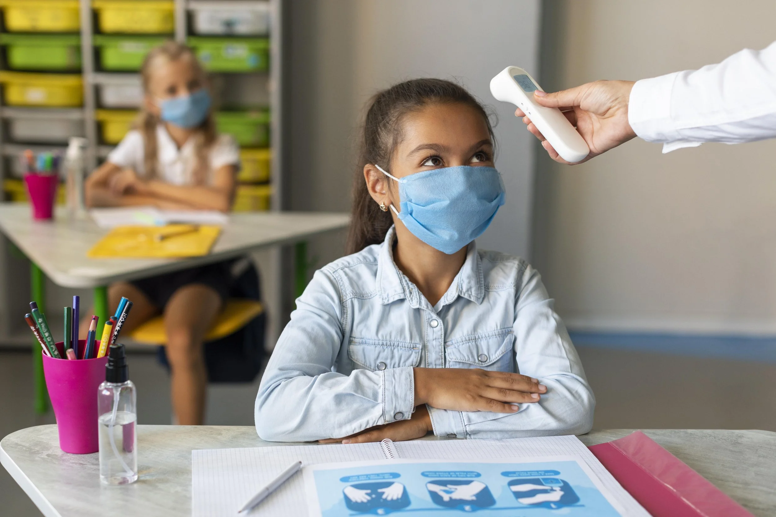 a kid getting her temperature checked while sitting in classroom