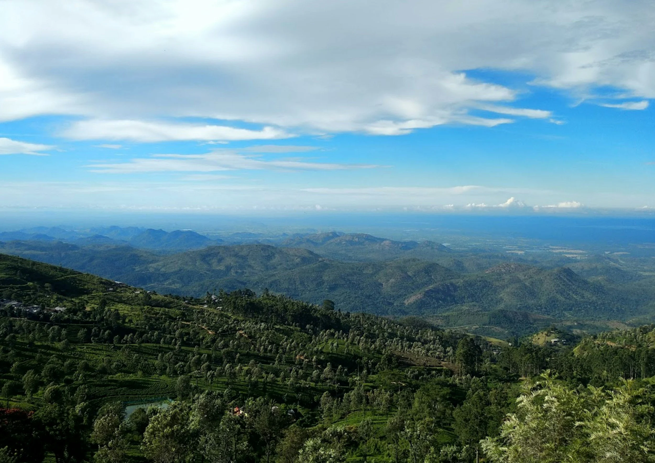 Vista panorámica de montañas verdes y nubes en el cielo con un paisaje agrícola en primer plano.