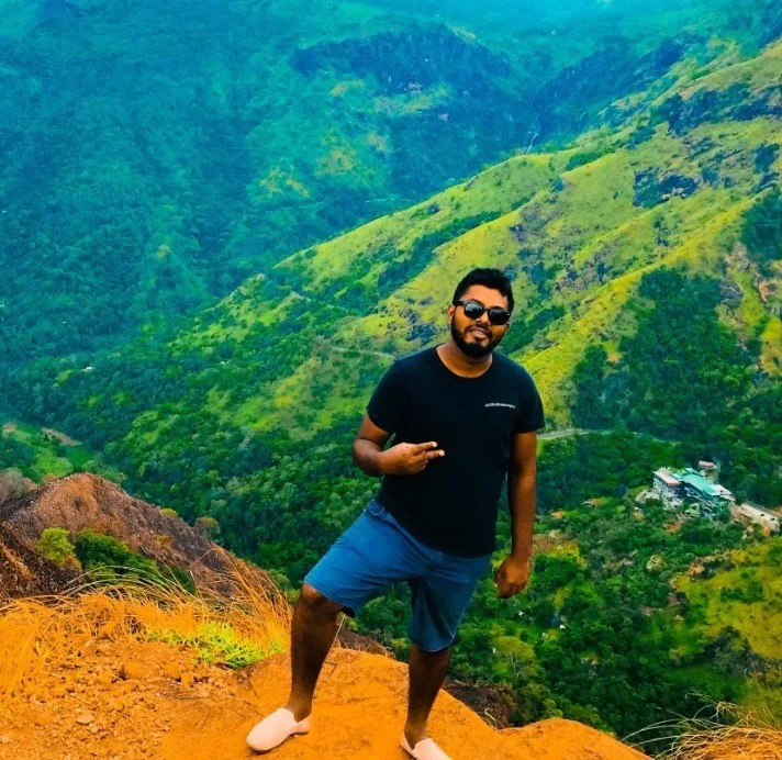 Hombre de pie en una cima de montaña con paisaje verde de fondo.