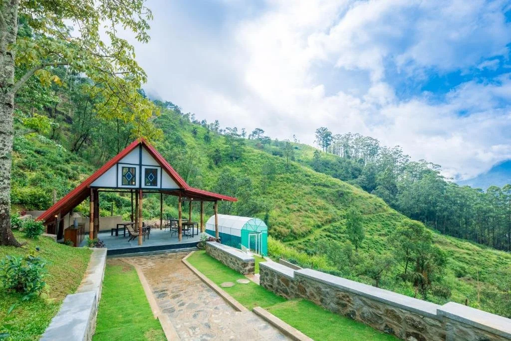 Casa de madera con techo rojo en colina verde con caminos y paisaje montañoso.