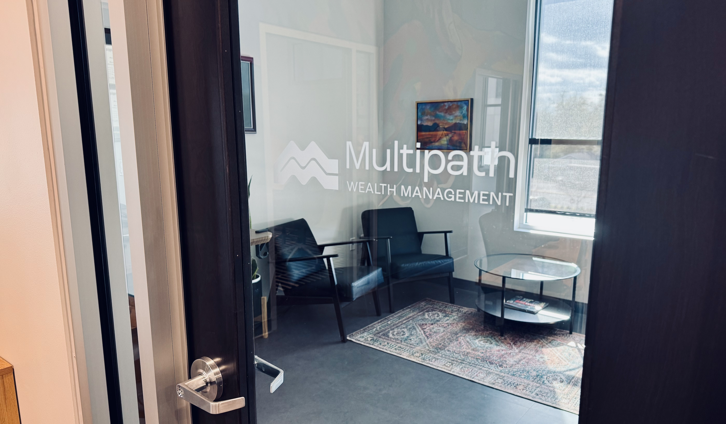 Office door with business name Multipath Wealth Management visible on the glass panel. Through the glass you can see office furniture and a window.