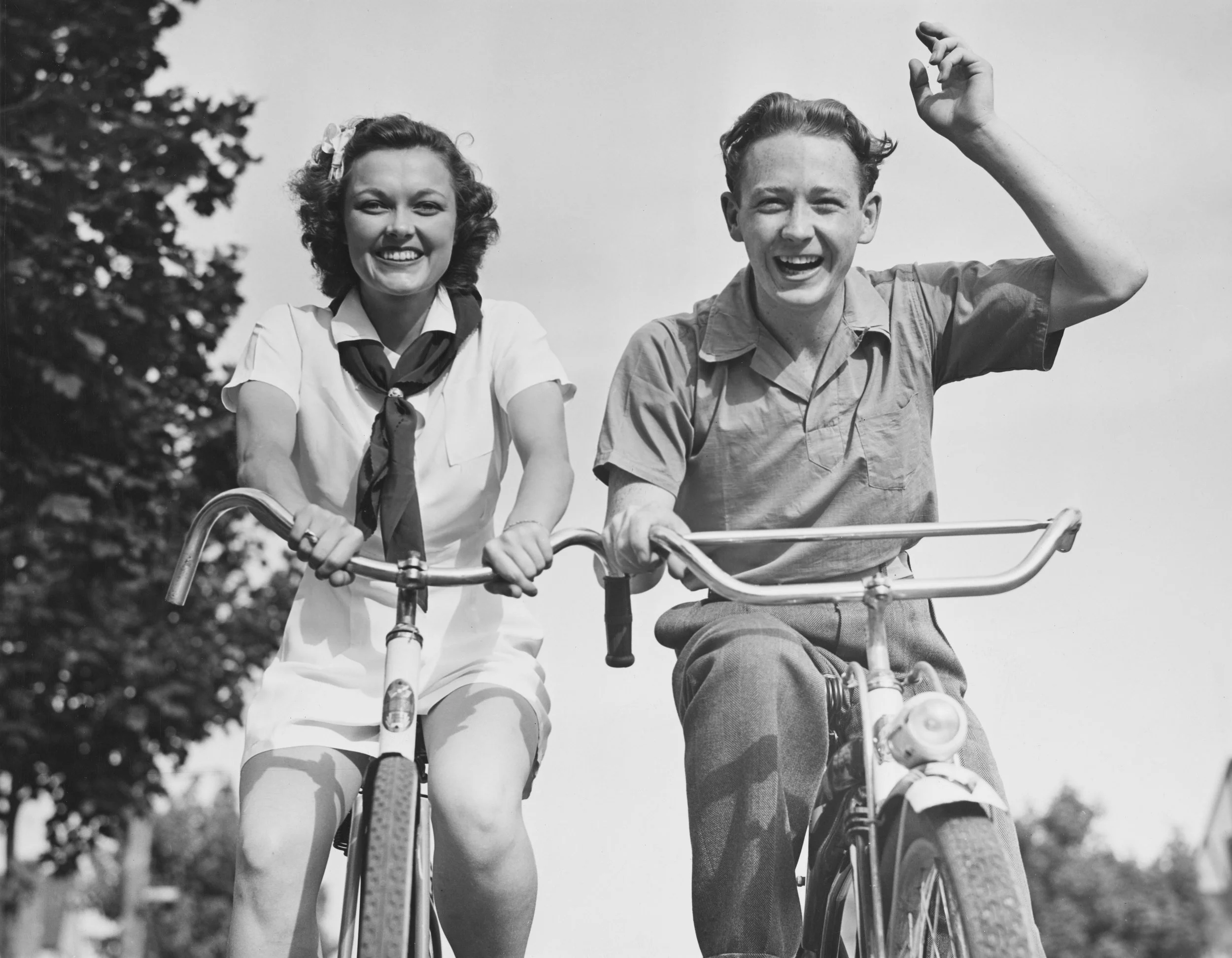 Deux jeunes enfants, une fille et un garçon, souriants, faisant du vélo ensemble dans un cadre en plein air.