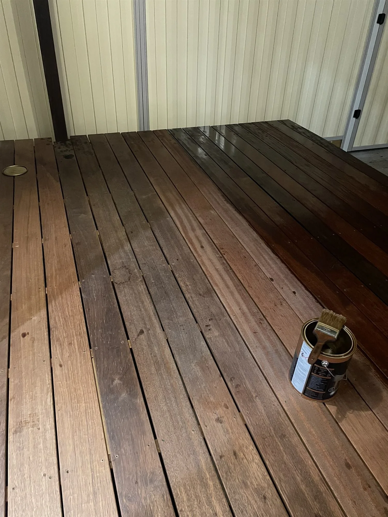 Deck oil being applied by brush to covered timber deck boards
