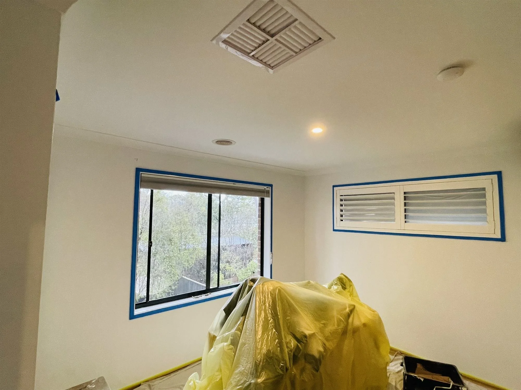 Nursery with window and shutters masked and furniture covered before painting