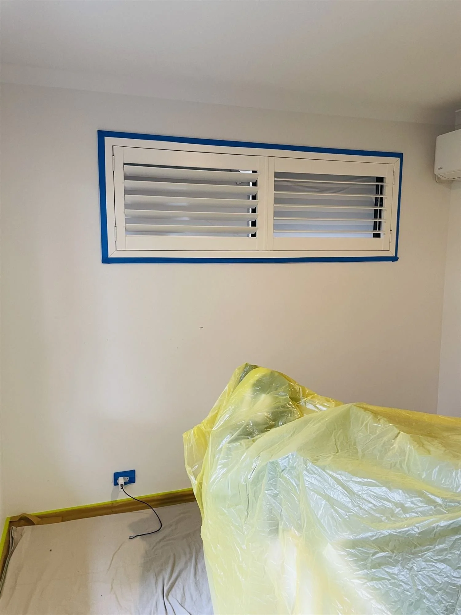 Plantation shutters masked with blue tape before nursery wall painting