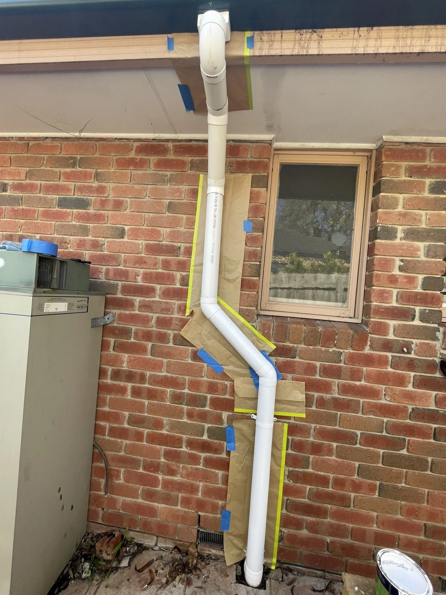 White PVC downpipe masked and ready for painting on a brick house