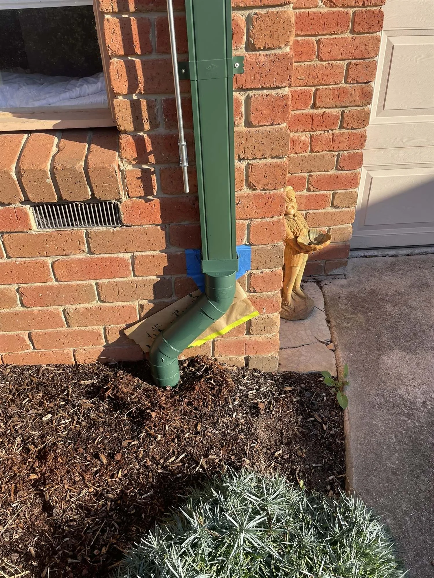 Close-up of a dark green painted downpipe at ground level