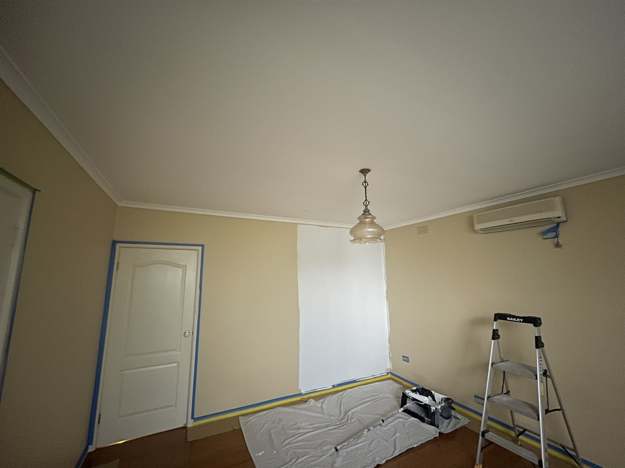 Beige room partway through a repaint, with a fresh neutral section beside the door