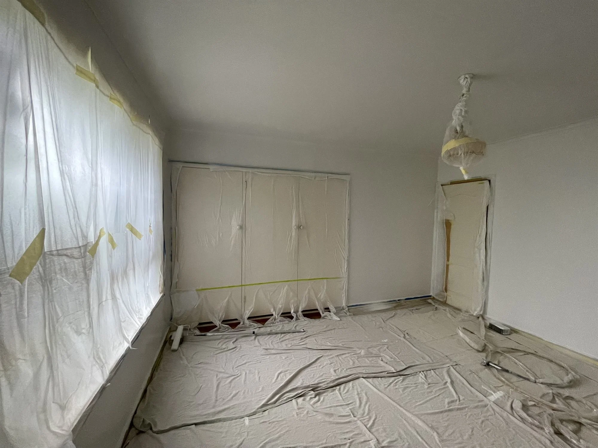 Bedroom with wardrobes, windows and floor fully masked before repainting