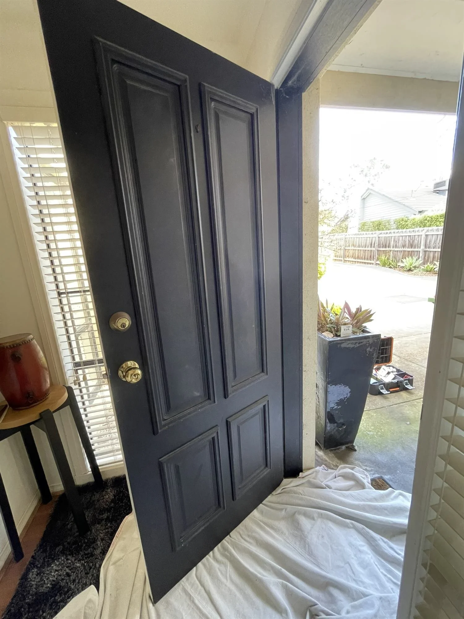 Front door freshly painted in black gloss, with the floor protected by a drop sheet