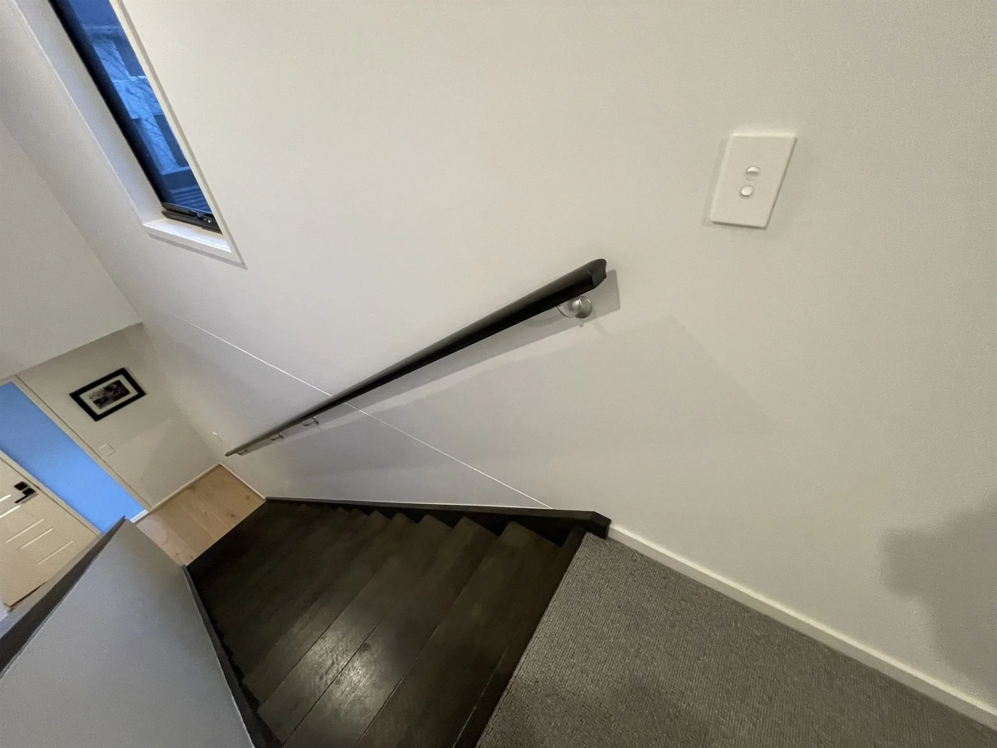 Staircase with dark timber treads beside a freshly painted white wall and handrail