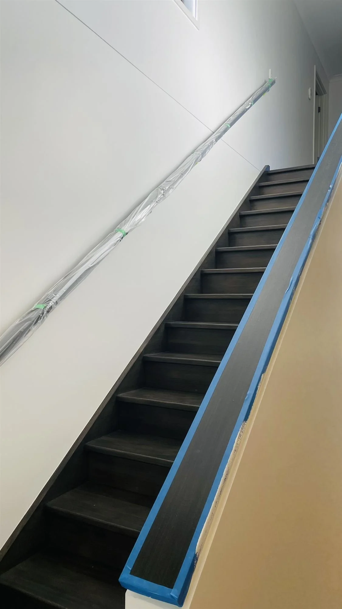 Balustrade capping masked with blue tape beside a staircase during painting