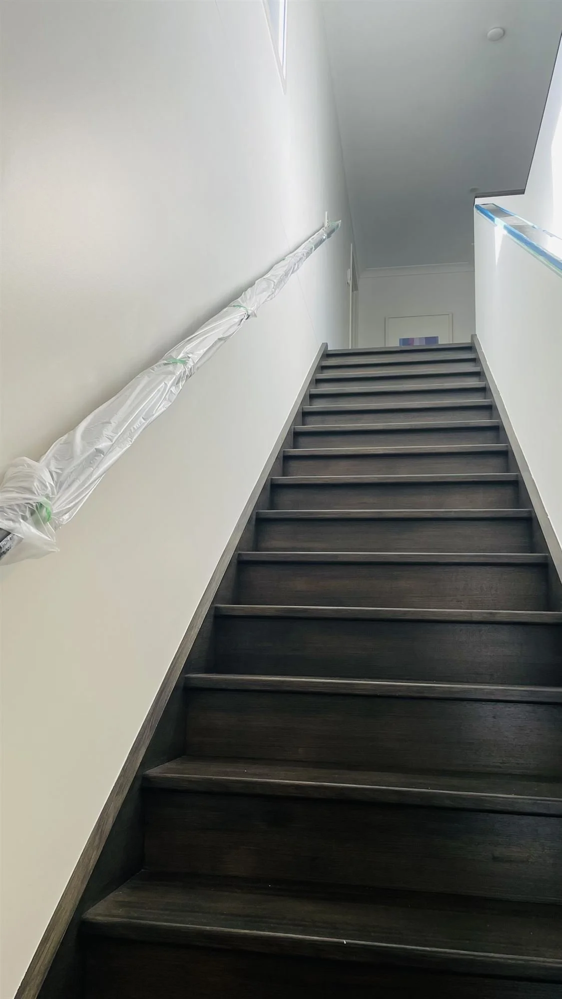 Stairwell walls painted white, with the handrail protected in plastic