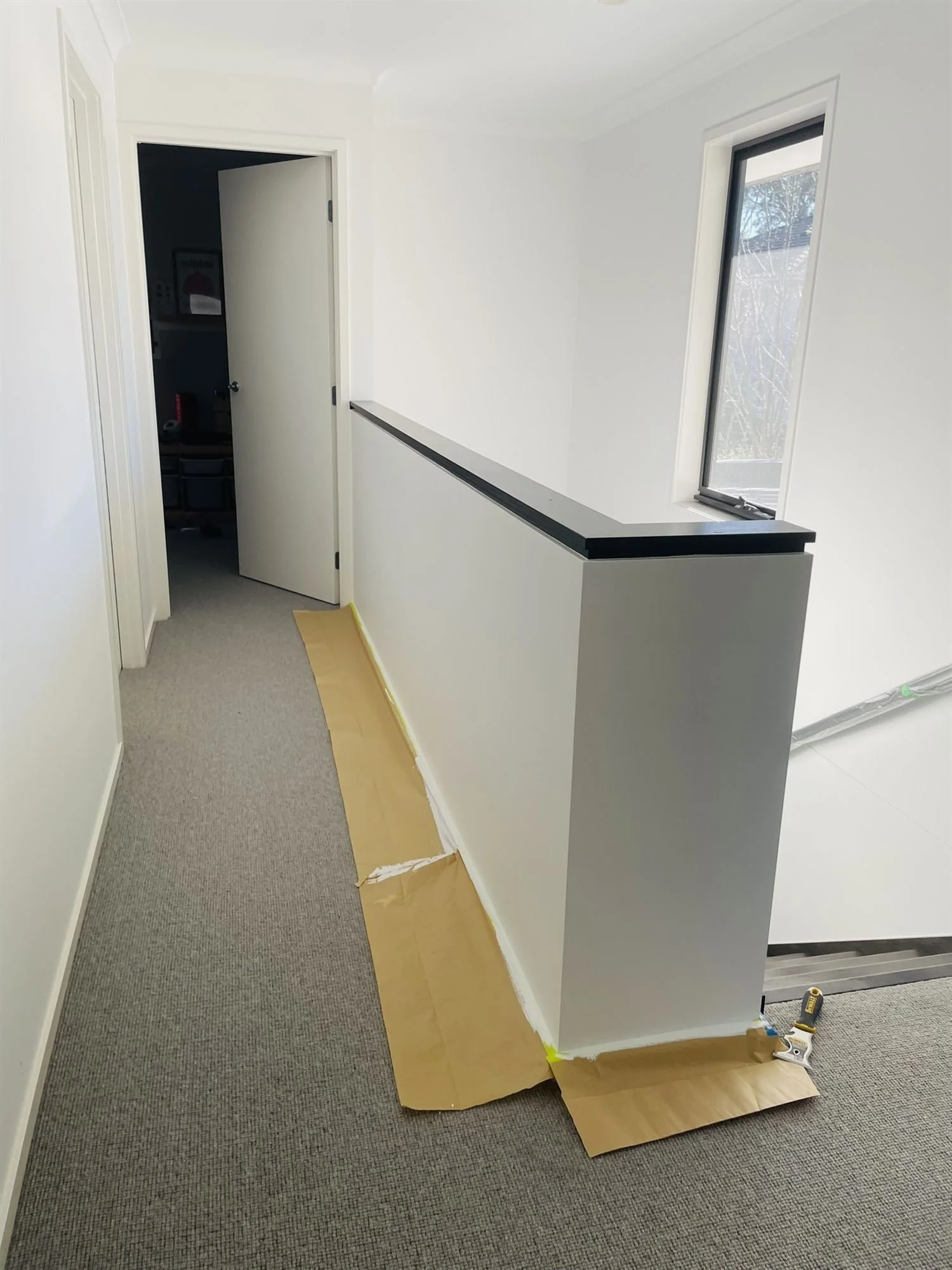 Upstairs landing balustrade painted white, with the carpet protected by masking paper