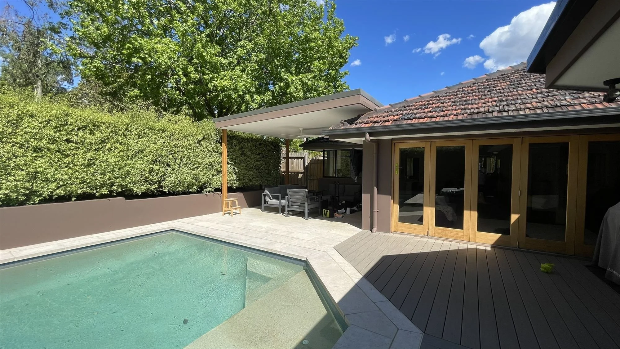 Rear of a home with clear-finished timber bifold and French doors beside a pool