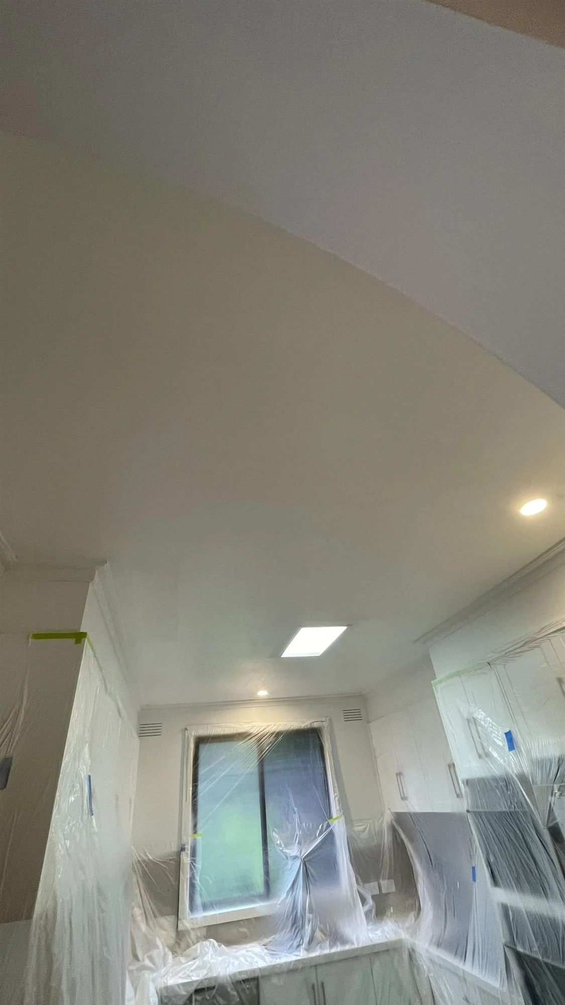 Kitchen cabinetry and window masked with plastic before painting