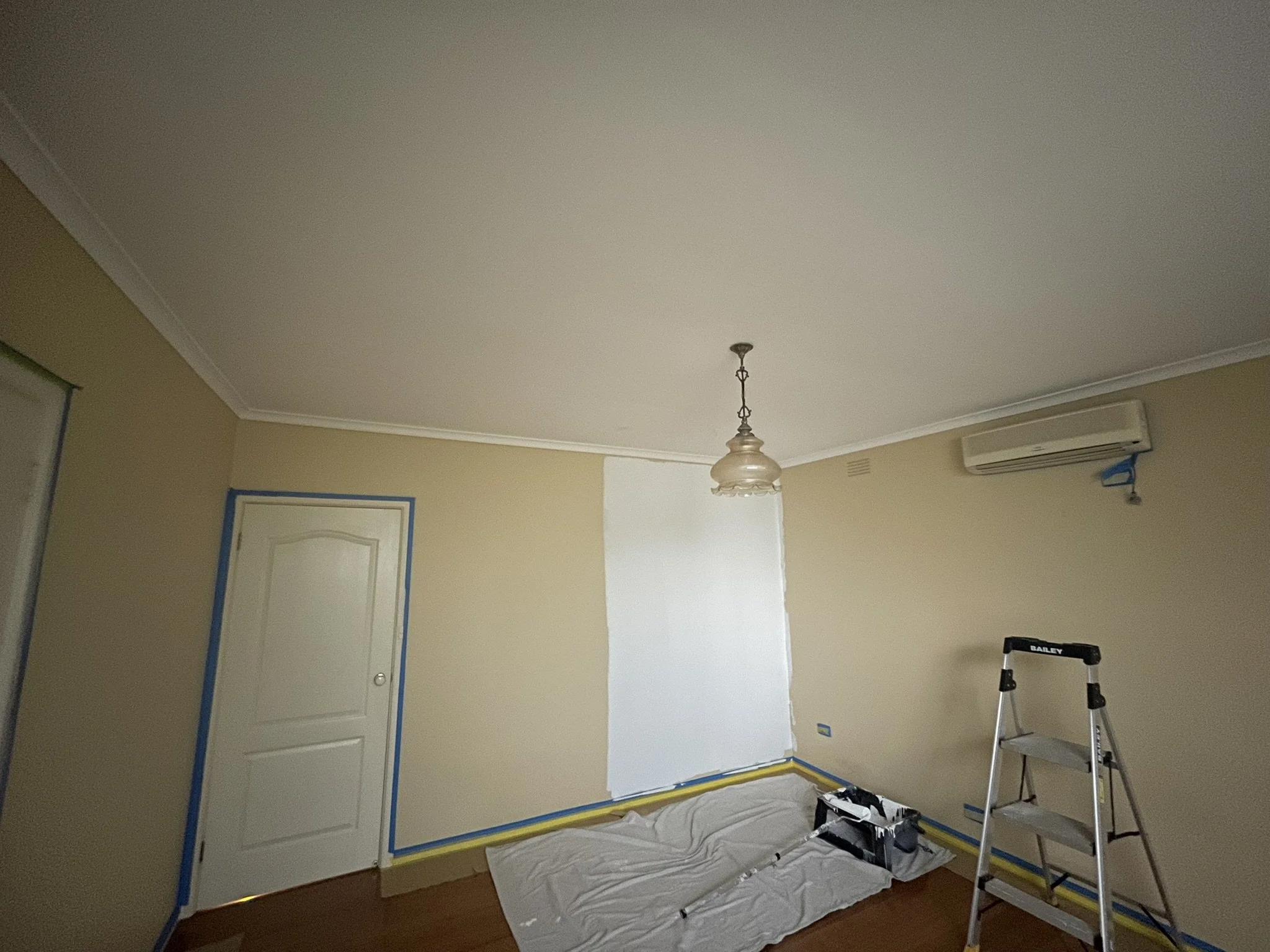 Beige room partway through a repaint, with a fresh neutral section beside the door