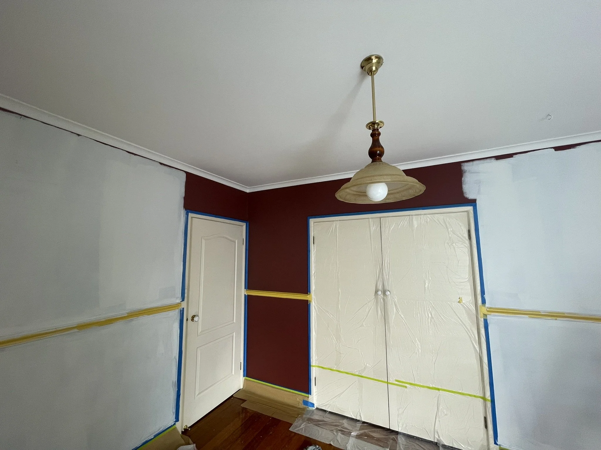 Dark red bedroom partly repainted in a neutral colour, with doors and floors protected