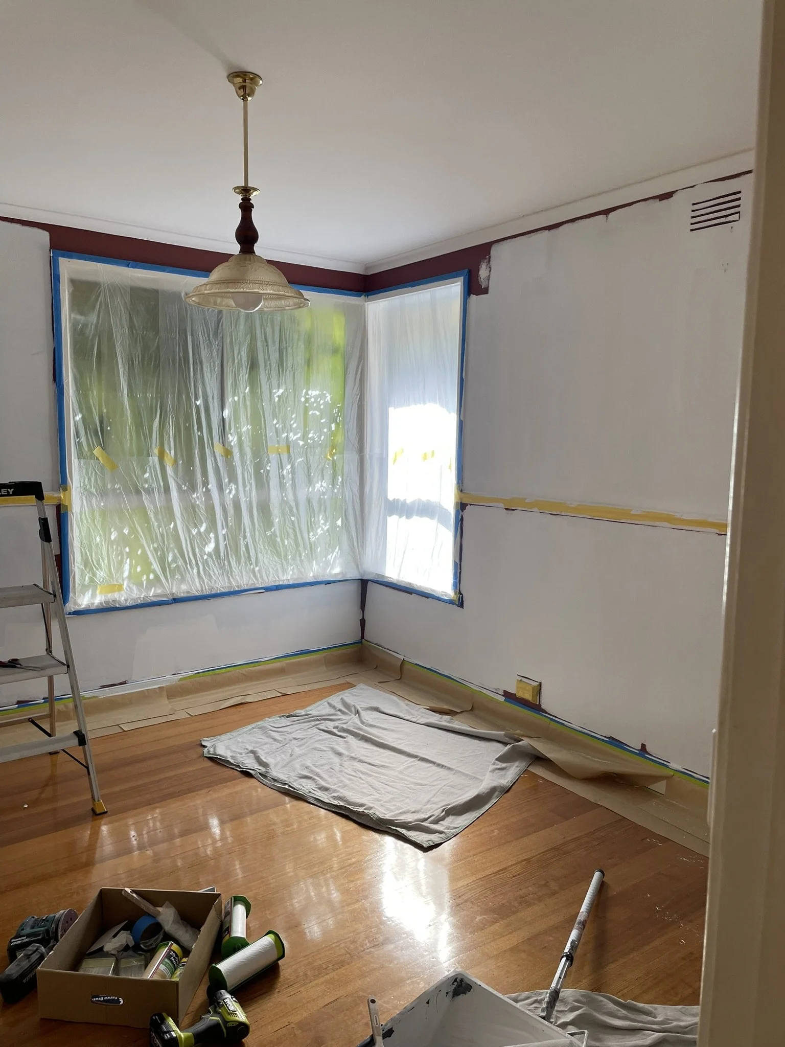 Bay window masked with plastic while walls are cut in during an interior repaint